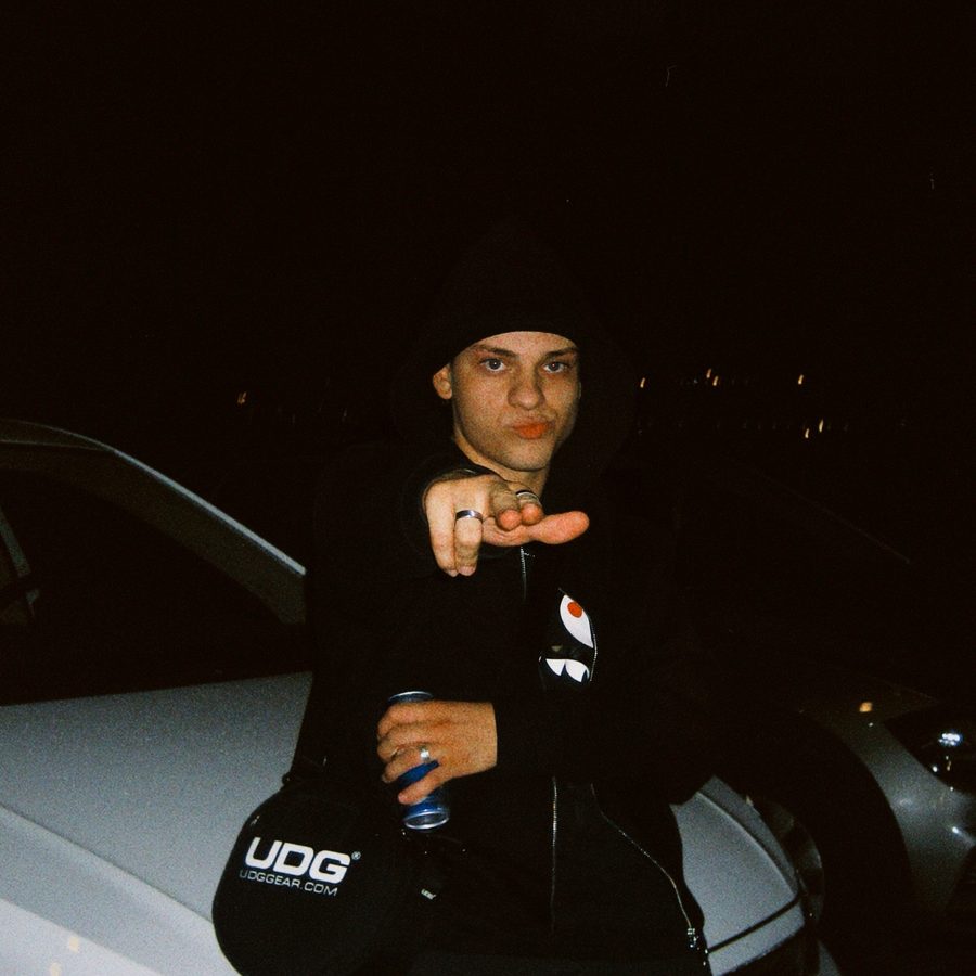 NYCO at night leaning on a white car, pointing at the camera