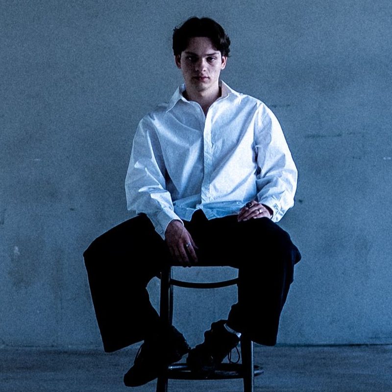 NYCO in a white shirt on a chair in an empty concrete room
